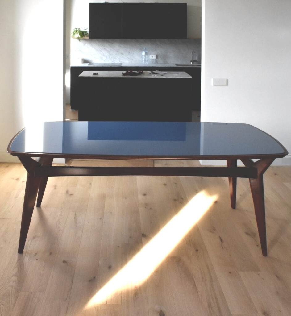 Tavolo snello e curvo in legno con gambe sagomate e piano in cristallo celeste