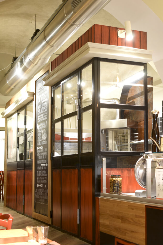 Parete divisoria tra cucina a vista e sala ristorante in ferro nero, vetro trasparente e pannelli in legno rosso sporcoArredamento su misura , Arezzo