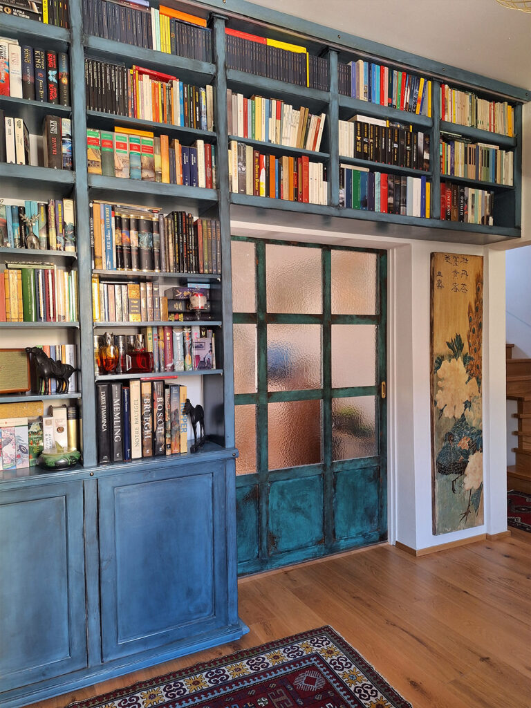 Libreria artigianale azzurra con ante invecchiate e vetrata interna in un salotto elegante