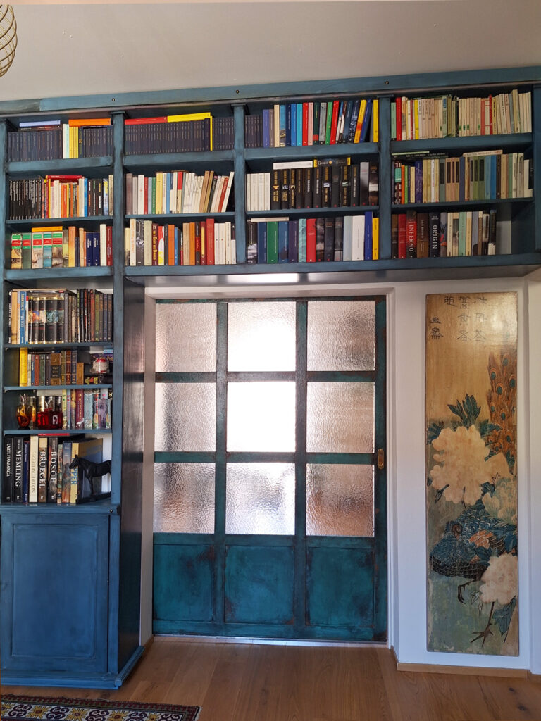 Libreria artigianale azzurra con ante invecchiate e vetrata interna in un salotto elegante